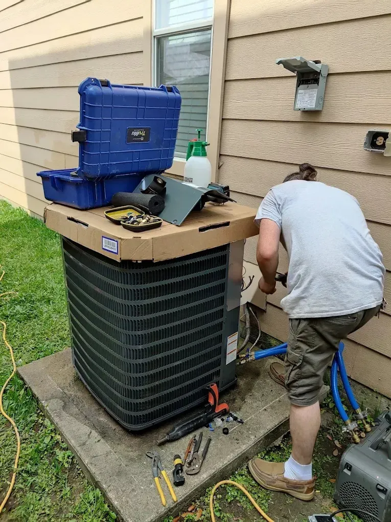 Technician working on an outdoor air conditioning unit beside tools and equipment.