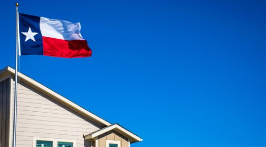 Texas State Flag the Symbol of the Lone Star State above Modern Brand New Suburban Home with blue sky and perfect sunny lighting